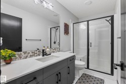 Bathroom featuring a spacious vanity with an undermount sink, a large mirror, and a walk-in shower with a frameless glass enclosure - 