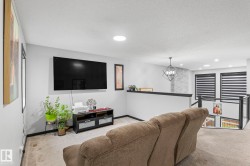 Carpeted living area featuring a wall-mounted media console, a television installation, and a round overhead light fixture - 