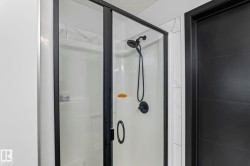 Shower enclosure with black-framed glass doors, white shower pan, and matte black shower fixtures - 