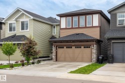 Contemporary brown and cream facade featuring stone veneer accents, a two-car garage, and multiple upper-level windows - 
