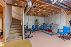 Unfinished basement featuring exposed wood joists, utility ductwork, and insulated wall framing, with a wooden staircase providing access - 