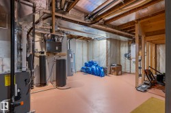 Unfinished basement space featuring exposed ceiling joists and ductwork, utility sink, water heater, water softener, and HVAC system - 