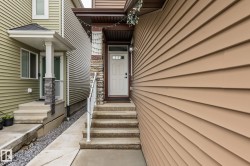 Front entrance featuring a white panel door with glass inserts, stone veneer accents, and concrete steps with a white handrail - 