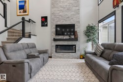 Two-story living area featuring a stacked stone fireplace with a black mantel and integrated linear electric fireplace - 