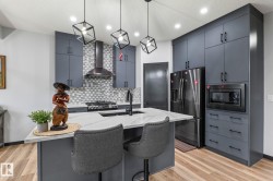 Modern kitchen featuring gray flat-panel cabinetry, a central island with a light-toned countertop, stainless steel appliances, and a mosaic tile backsplash - 