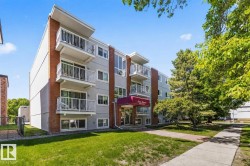 Multi-story building exterior featuring a red brick facade, light grey siding, and multiple balconies with white railings - 