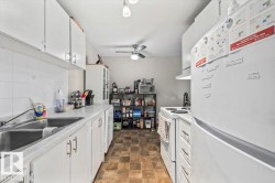 Galley kitchen featuring white cabinetry, a double basin stainless steel sink, white countertops, and a white tile backsplash - 