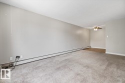 Spacious room featuring neutral wall tones, textured carpeting, baseboard heating, and a ceiling fan with integrated lighting - 