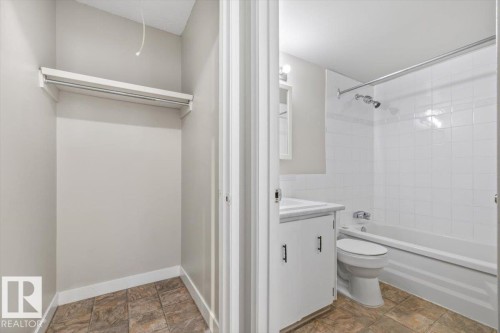 Bathroom featuring a white vanity with integrated sink, chrome faucet, white tiled shower and tub combination, and ceramic tile flooring - 306 10330 113 Street, Edmonton, AB 