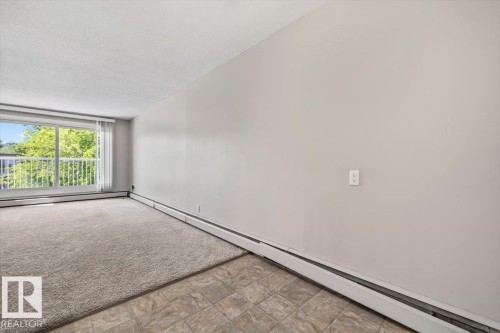 Bright living space featuring a full-width window with vertical blinds, providing abundant natural light - 306 10330 113 Street, Edmonton, AB 