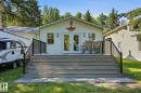 Rear exterior featuring white vinyl siding, a gabled roofline, a spacious deck with composite decking, black metal railings, and dual glass-paned doors - 1410 47436 Range Rd. 15, Rural Leduc County, AB 