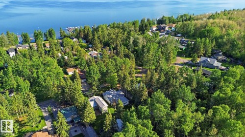Aerial perspective showcasing a residential area bordered by a large body of water, featuring dense tree coverage - 1410 47436 Range Rd. 15, Rural Leduc County, AB 