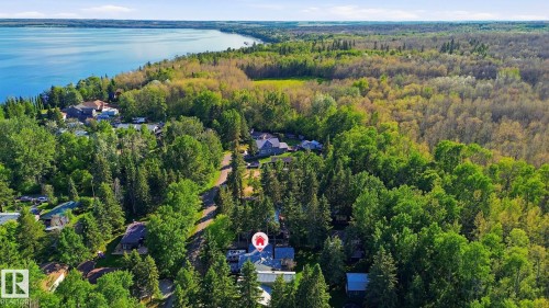 Expansive aerial showcasing a residential area bordered by a large body of water and dense mature tree cover - 1410 47436 Range Rd. 15, Rural Leduc County, AB 