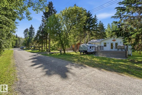 White exterior with a grey composite deck, surrounded by mature trees - 1410 47436 Range Rd. 15, Rural Leduc County, AB 