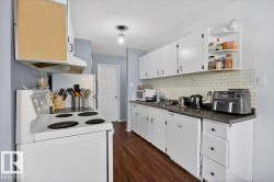 Kitchen featuring wood-finish flooring, white cabinetry, dark countertops, and a white subway tile backsplash - 