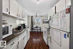 Galley kitchen featuring white cabinetry, dark countertops, and a white subway tile backsplash - 