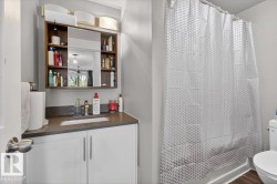 Bathroom featuring a white vanity with a dark countertop, an integrated sink, a wall-mounted mirrored medicine cabinet, and a shower with a white tub surround - 