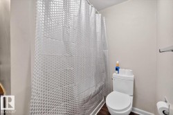 Full bathroom featuring a white toilet, wood-finish flooring, and a shower/tub combination with a white shower curtain - 