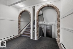 Brick archways accent the entryway, featuring textured white walls, a dark patterned carpet, and built-in baseboard heating - 