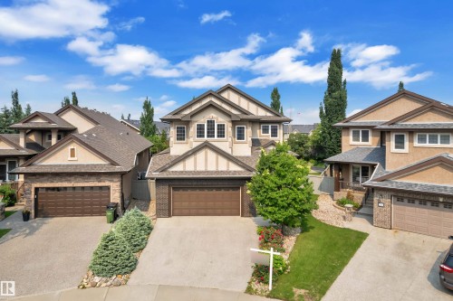 Two-story residential exterior featuring a prominent gabled roofline, stucco and brick facade, a two-car garage with a brown door, and a paved driveway - 2422 Warry Place, Edmonton, AB 