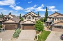Two-story residential exterior featuring a prominent gabled roofline, stucco and brick facade, a two-car garage with a brown door, and a paved driveway - 2422 Warry Place, Edmonton, AB 