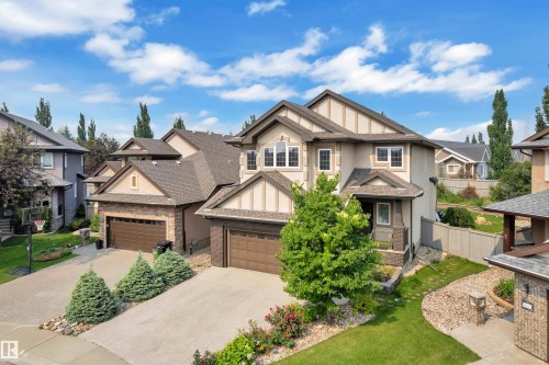 Rear exterior featuring a spacious lawn, circular paver patio, wood deck, and established garden beds with various plantings - 2422 Warry Place, Edmonton, AB 