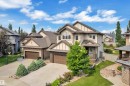 Rear exterior featuring a spacious lawn, circular paver patio, wood deck, and established garden beds with various plantings - 2422 Warry Place, Edmonton, AB 