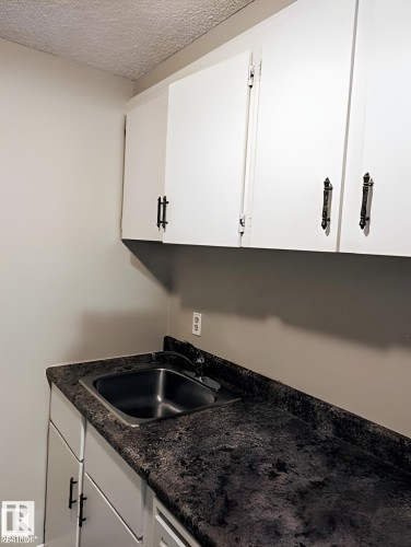 Utility area featuring a stainless steel sink, dark speckled countertop, and white cabinetry with black hardware - 611 12831 66 Street, Edmonton, AB 