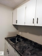 Utility area featuring a stainless steel sink, dark speckled countertop, and white cabinetry with black hardware - 