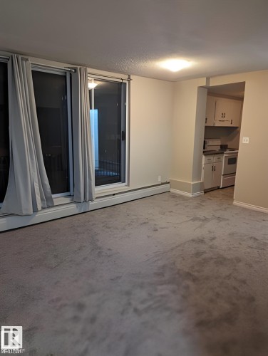 Sliding glass doors with window treatments, recessed kitchen area with white cabinetry, wall-to-wall carpeting, and neutral wall paint - 611 12831 66 Street, Edmonton, AB 