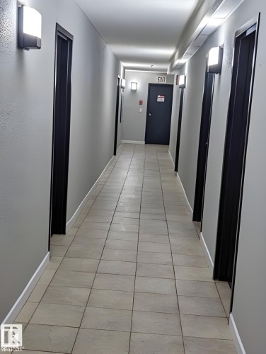 Hallway with light gray walls, dark door frames, and sconce lighting - 611 12831 66 Street, Edmonton, AB 