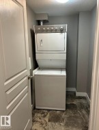 Dedicated laundry area featuring a stacked washer and dryer unit, gray wall paint, white baseboards, and patterned flooring - 