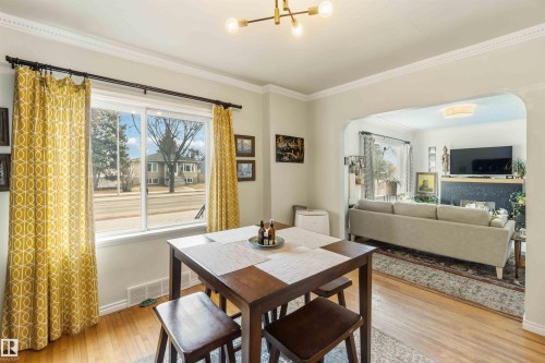 Hardwood-finish flooring throughout, featuring a large window with white trim, a modern ceiling light fixture, and crown molding - 6036 106 Street, Edmonton, AB 