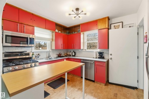 Bright kitchen featuring red cabinetry, stainless steel appliances, a breakfast bar, white subway tile backsplash, and cork flooring - 6036 106 Street, Edmonton, AB 