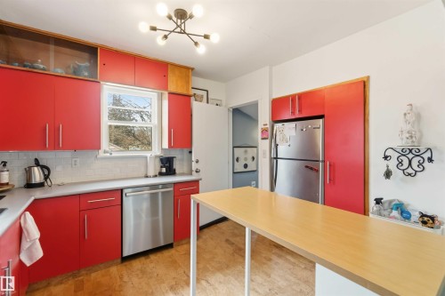 Kitchen featuring red cabinetry, wood-finish flooring, stainless steel appliances, a white subway tile backsplash, and a modern ceiling light fixture - 6036 106 Street, Edmonton, AB 