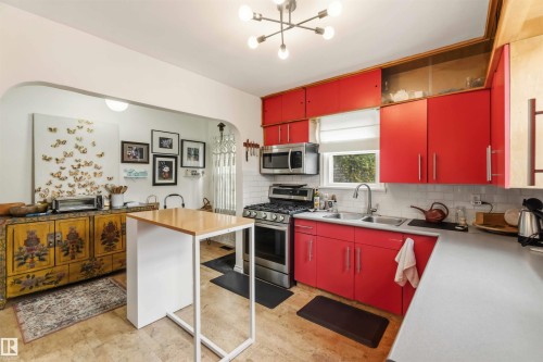 Modern kitchen featuring vibrant red cabinetry, stainless steel appliances, a subway tile backsplash, and a double basin sink - 6036 106 Street, Edmonton, AB 