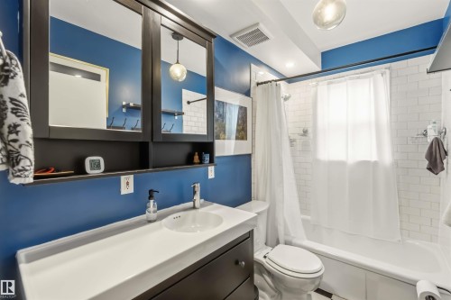 Bathroom featuring a dark wood-finish vanity with an integrated white sink, a coordinating medicine cabinet with mirrored doors, a white subway tile surround, a built-in bathtub, and a window - 6036 106 Street, Edmonton, AB 