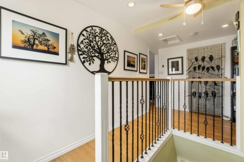 Upper-level hallway featuring wood-finish flooring, wrought iron balusters with decorative twists, a light-toned wood handrail, recessed lighting, and a ceiling fan - 6036 106 Street, Edmonton, AB 