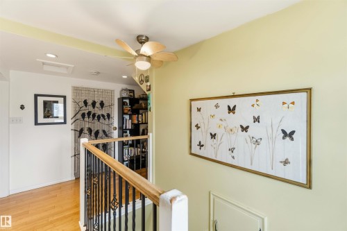 Wood-finish flooring and a staircase featuring wrought iron balusters with a wood handrail - 6036 106 Street, Edmonton, AB 
