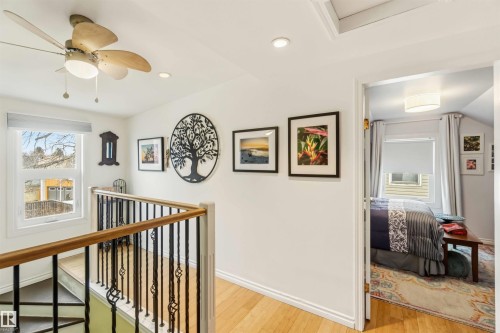 Hardwood flooring throughout a bright upper-level hallway featuring a ceiling fan with integrated lighting, recessed lighting, and a window with a roller shade - 6036 106 Street, Edmonton, AB 