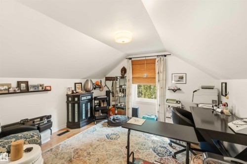 Attic room featuring sloped ceilings, a window with a woven wood shade, wood-finish flooring, a built-in wall shelf, and a flush-mount ceiling light fixture - 6036 106 Street, Edmonton, AB 