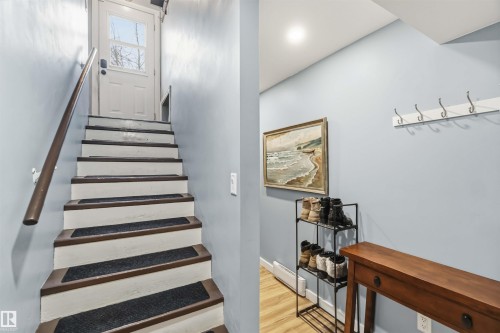 Staircase with wood-finish treads and white risers, featuring a wood-finish handrail and a windowed door providing natural light - 6036 106 Street, Edmonton, AB 