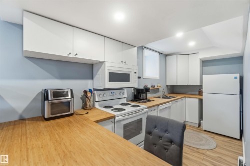 Kitchen featuring white cabinetry, light wood-finish countertops, stainless steel sink with a single-handle faucet, and white appliances - 6036 106 Street, Edmonton, AB 