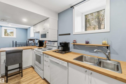Kitchen featuring wood-finish countertops, dual basin stainless steel sink, and white cabinetry - 6036 106 Street, Edmonton, AB 