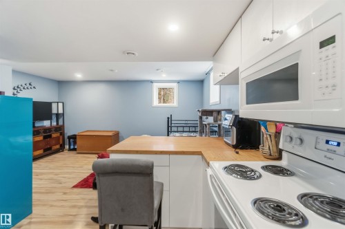Kitchenette featuring white cabinetry, a built-in microwave, and a white electric range with a light wood-finish countertop that extends to a breakfast bar - 6036 106 Street, Edmonton, AB 