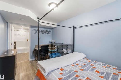 Room featuring wood-finish flooring, a built-in light fixture, and a doorway leading to an additional space with a bathtub and tiled walls - 6036 106 Street, Edmonton, AB 