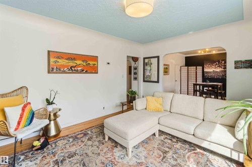 Living area featuring wood-finish flooring, a light blue textured ceiling, and an arched doorway leading to an adjacent room - 6036 106 Street, Edmonton, AB 