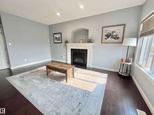 Living area featuring a central fireplace with an arched alcove, dark wood-finish flooring, and light-toned walls - 108 South Creek Wynd, Stony Plain, AB 