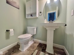 Bathroom featuring a white pedestal sink with a contemporary faucet, a round wall-mounted mirror, and wood-finish flooring - 