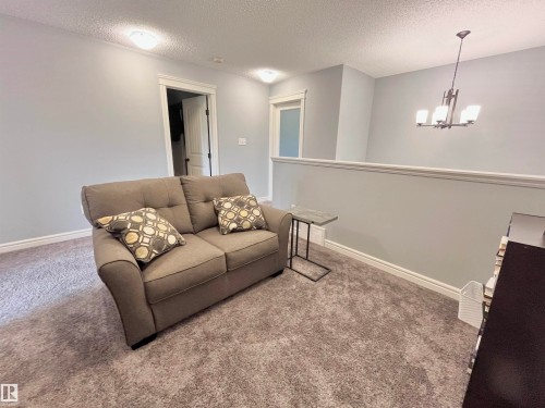 Carpeted upper-level landing featuring a light gray painted half-wall with white trim, a decorative chandelier, and two recessed ceiling lights - 108 South Creek Wynd, Stony Plain, AB 